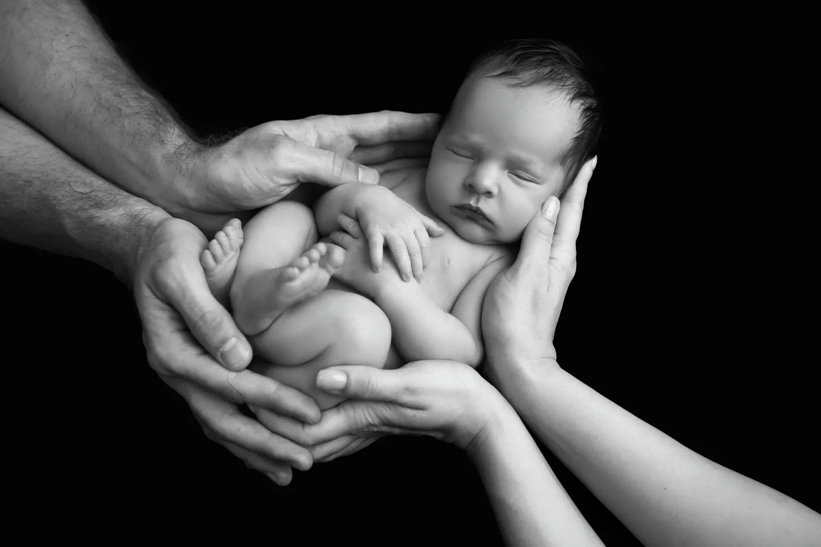 Crno-bijela fotografija novorođenčeta u rukama roditelja — Newborn Studio Devine